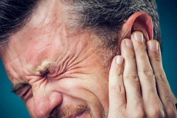 A man with short hair closes his eyes tightly in pain and presses his hand against his ear, suggesting discomfort or earache.