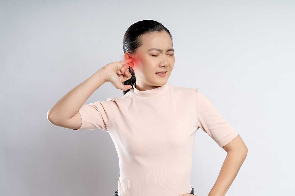 Woman in a pink top pressing on her ear and wincing from a clogged ear, a concern Carson Hearing Care addresses in Fort Worth, TX